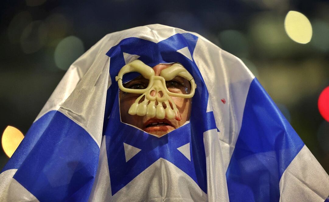 Un manifestante con una máscara y envuelto en una bandera israelí asiste a una protesta en Tel Aviv, el 3 de mayo de 2025, para exigir la liberación de rehenes israelíes cautivos, desde los ataques del 7 de octubre perpetrados por militantes palestinos, en la Franja de Gaza y el fin de la guerra.