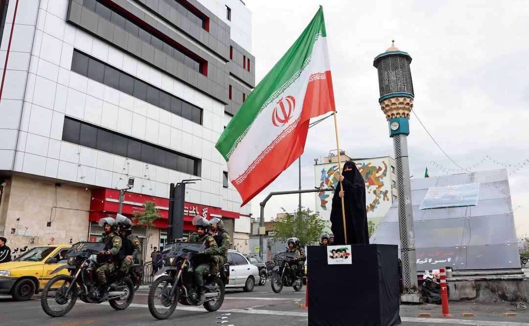 Fuerzas de seguridad iraníes pasan junto a una mujer que ondea la bandera nacional en Teherán. Foto: EFE
