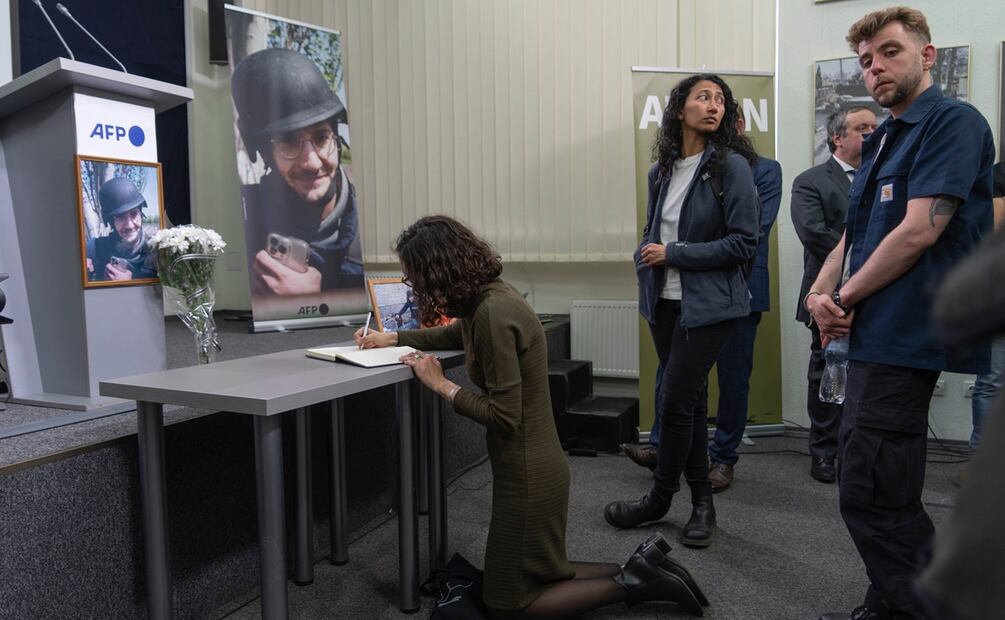 Un colega escribe en un libro de recuerdos durante una ceremonia de conmemoración en Kiev, Ucrania, mientras otros reporteros esperan su turno junto a una pantalla que muestra una fotografía que muestra al periodista de la AFP Arman Soldin. Foto: AP