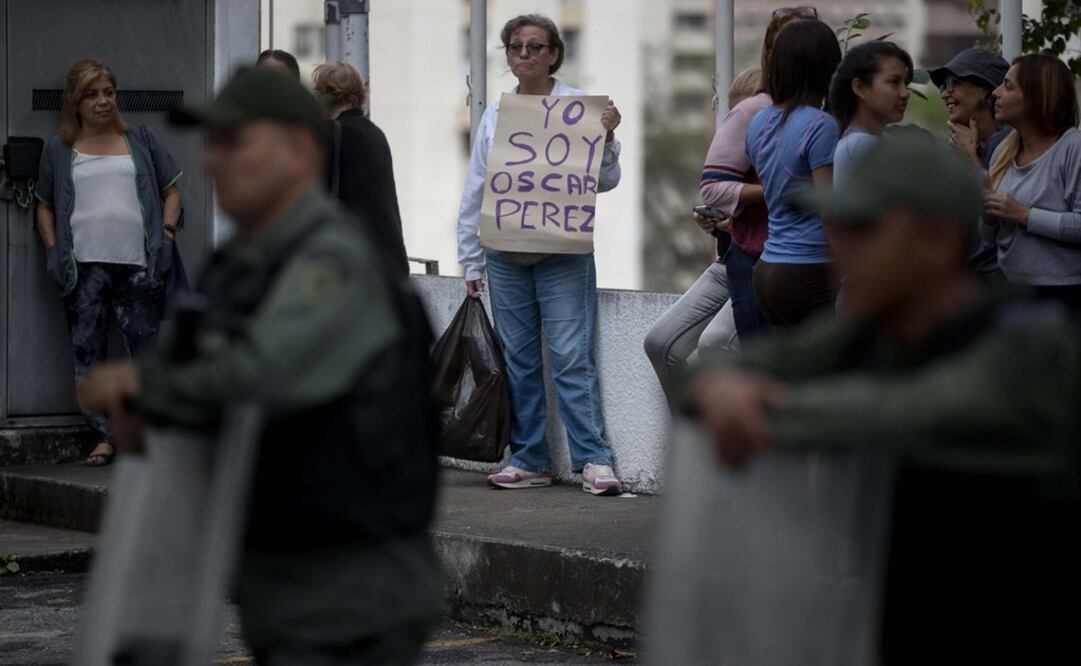 Una mujer sostiene un cartel en el que se lee "Yo soy Oscar Pérez" frente a miembros de la Guardia Nacional Bolivariana y la Policía Nacional Bolivariana que custodian las inmediaciones de la morgue (Foto: EFE)