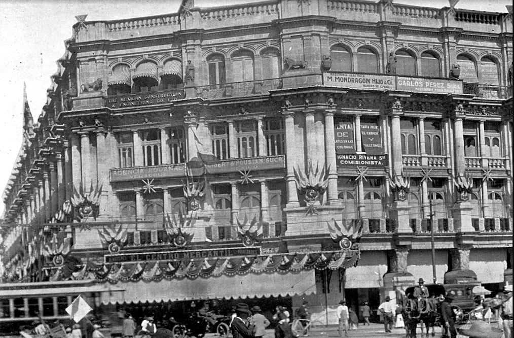 El enorme edificio del Centro Mercantil adornado para los Festejos de la Celebración del Centenario de la Independencia de México en una fotografía de septiembre de 1910. En los alrededores se aprecia la vida cotidiana a unos pasos del Zócalo Capitalino. Imagen: Col. Villasana-Torres