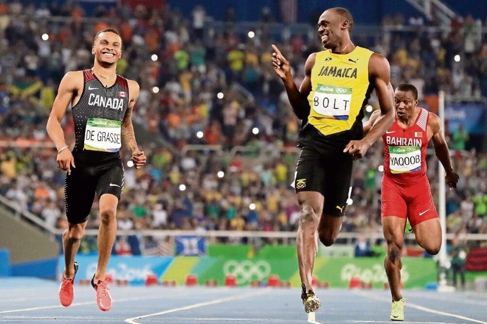 El canadiense André de Grasse intentó adelantarse en los metros finales a Usain, quien sonrió al verlo (DAVID J. PHILLIP. AP)