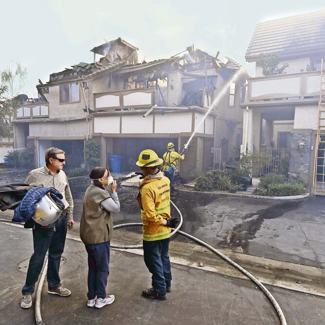 Sandro y Antoinette Zanon examinan el daño en Westlake Village, California, junto con un bombero de la ciudad de Los Ángeles, mientras las casas de sus vecinos arden por el fuego de Woolsey. (KEVORK DJANSEZIAN. AFP)