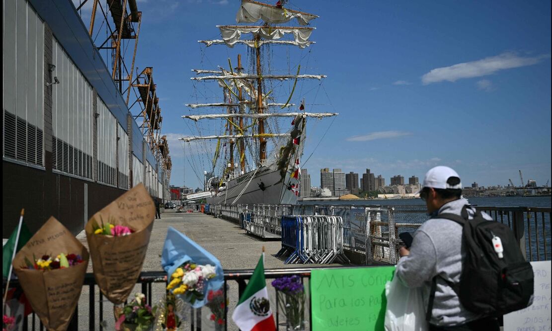 Un altar improvisado crece con mensajes de apoyo a las víctimas y sus familias en donde se observa al Buque Cuauhtémoc estacionado en el muelle de Nueva York, el lunes 19 de mayo de 2025, mientras se investiga el accidente en el que murieron dos tripulantes. Foto: AFP