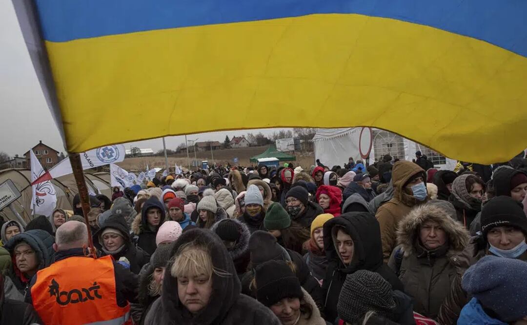 El voluntario Oleksandr Osetynskyi, sostiene una bandera ucraniana y dirige a cientos de refugiados tras huir de Ucrania y llegar al cruce fronterizo en Medyka, Polonia. Foto: AP 