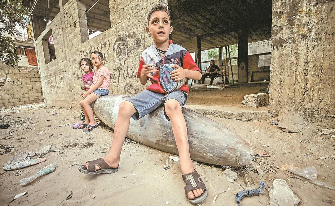 Niños palestinos se sientan en una bomba sin explotar lanzada por aviones de combate israelíes sobre la Ciudad de Gaza. Foto: Mohammed Saber/ EFE.