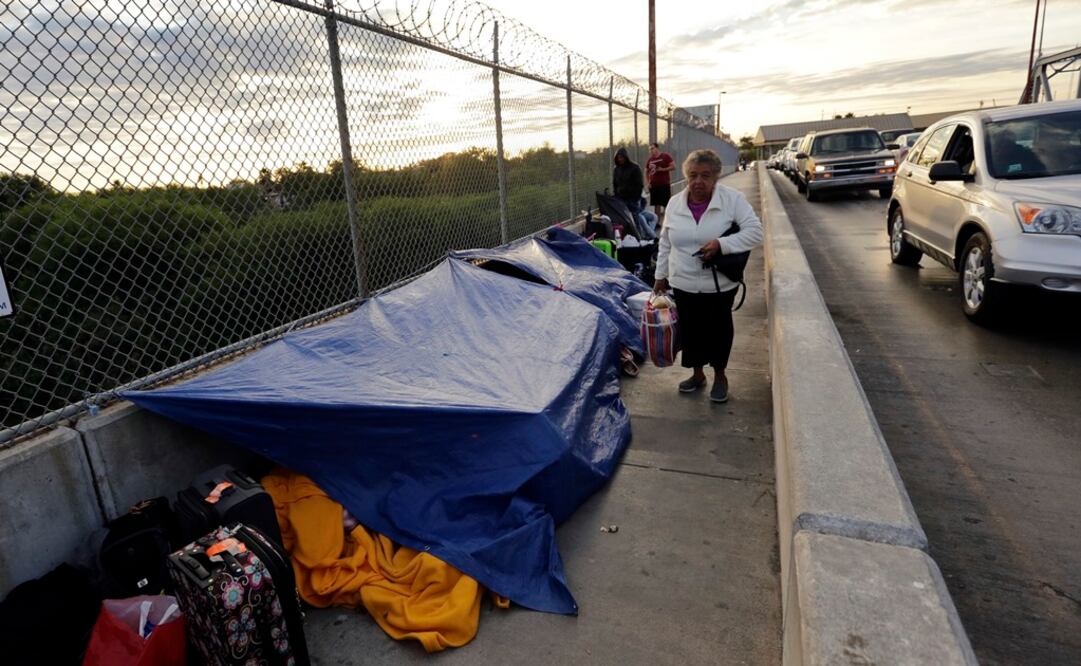 Los peatones pasan por inmigrantes que buscan asilo en los Estados Unidos, protegidos bajo una lona en el Puente Internacional de Brownsville y Matamoros. (Foto: AP)