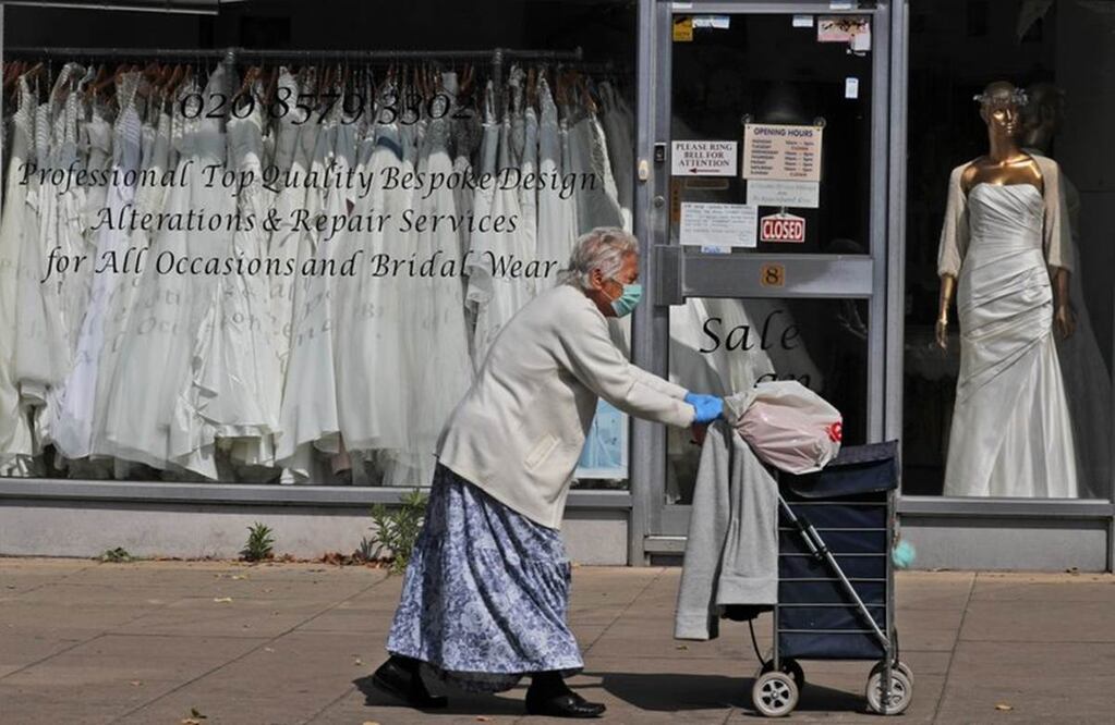 Una mujer camina frente a una tienda de vestidos de novia en Londres, donde las prendas sin vender se apilan en el escaparate. Las bodas en el Reino Unido se han pospuesto debido a la pandemia de COVID-19 .(AP Foto/Frank Augstein)