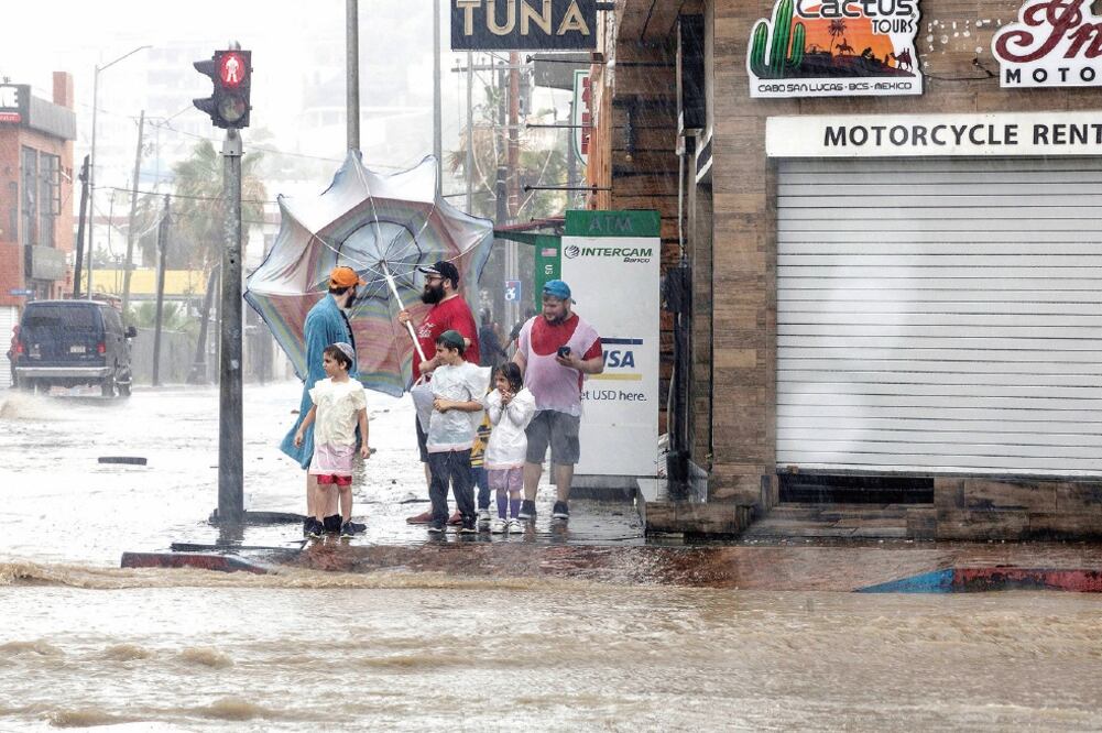 Unas personas se detienen cerca de una calle inundada mientras pasa la tormenta tropical, en Los Cabos, Baja California Sur. (REUTERS)