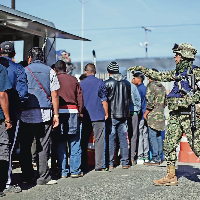 Los centroamericanos tienen que hacer largas filas para obtener un plato de comida, que preparan cocineros de la Marina; un oficial cuida el orden. (HANNAH MCKAY. REUTERS)