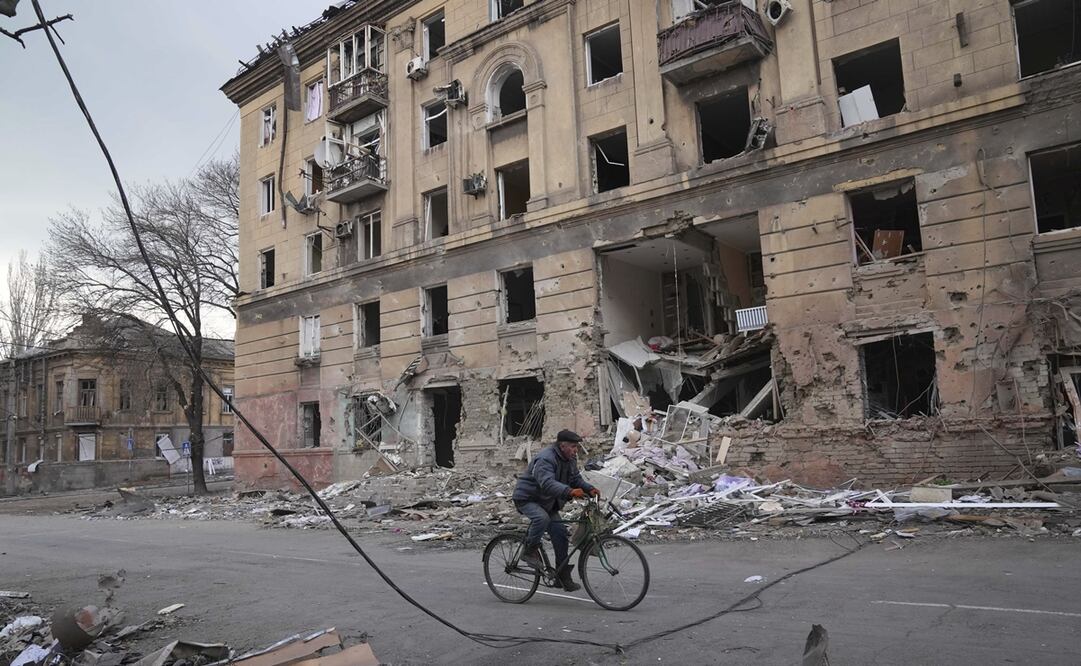 Un hombre monta en bicicleta frente a un edificio de apartamentos dañado por los bombardeos en Mariupol. Foto: AP