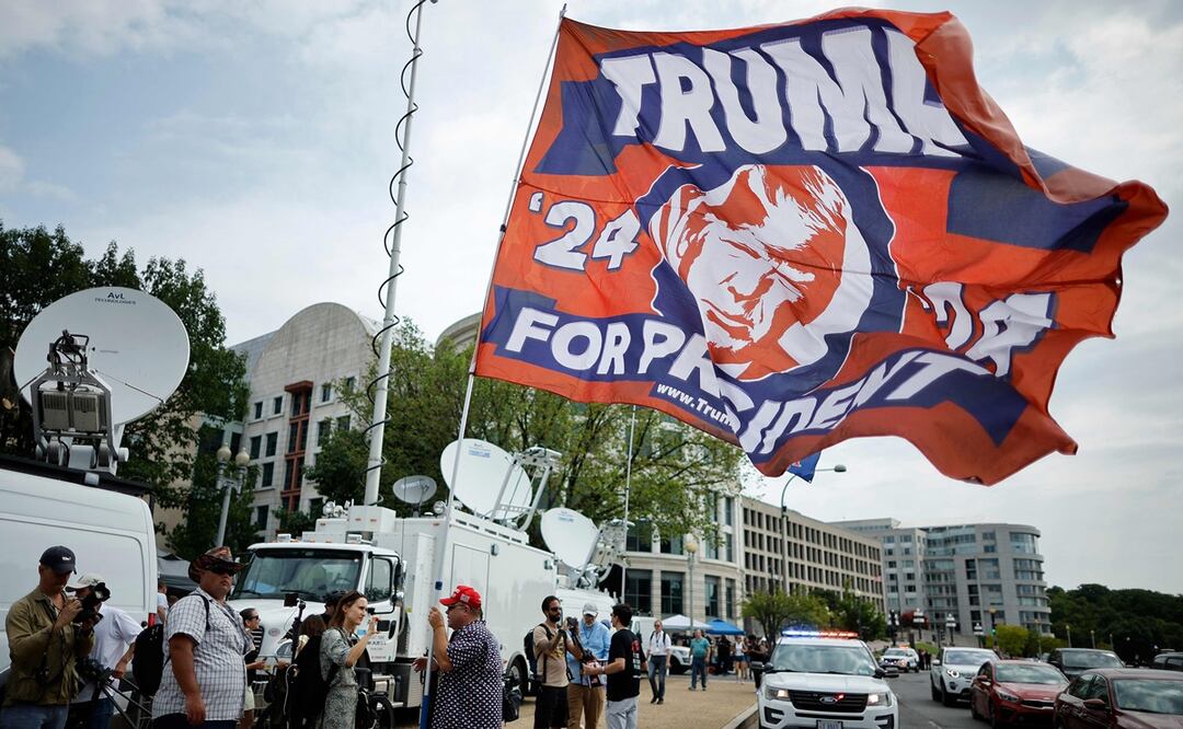 Un partidario lleva una gran bandera en apoyo de los camiones de televisión satelital de Donald Trump fuera del Tribunal de Distrito de los Estados Unidos. Foto: AFP
