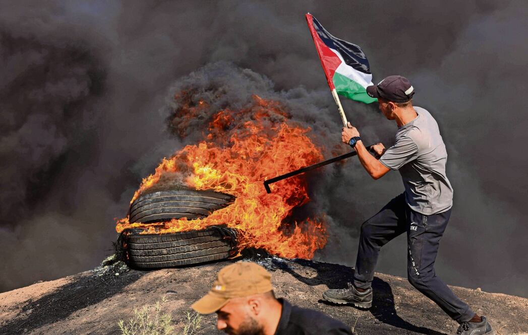 Un palestino sostiene una bandera junto a neumáticos en llamas durante una protesta en la valla fronteriza con Israel, al este de Gaza. Foto: Mahmud Jamones / AFP