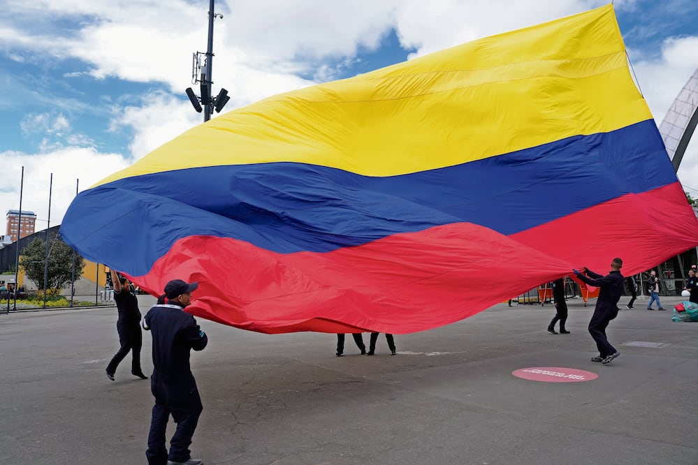 Trabajadores del centro de eventos Corferias izan la bandera nacional en Bogotá, un día después de la segunda vuelta de las elecciones presidenciales. Foto: Fernando Vergara/ AP