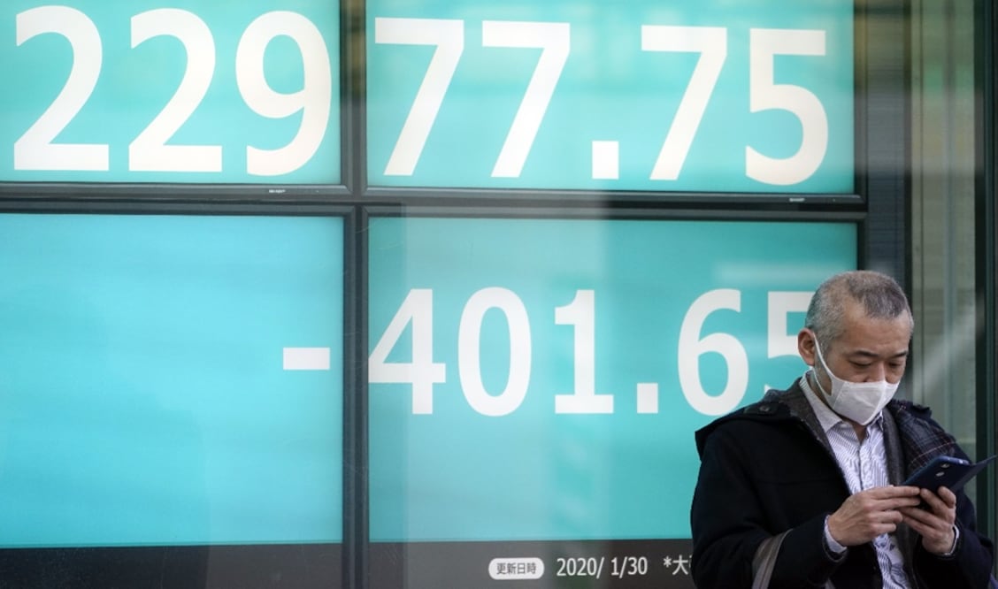 A man wearing a mask stands in front of a stock market indicator board - Photo: Frank Robichon/EFE