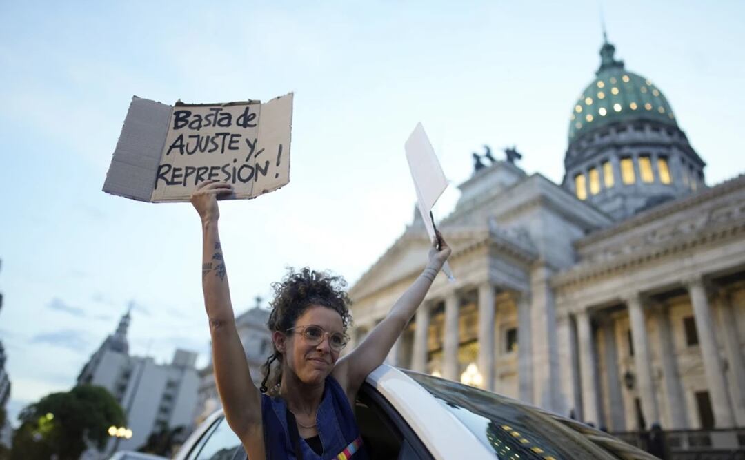 Una mujer se asoma por la ventana de un vehículo sosteniendo carteles de rechazo a la reforma económica promovida por el presidente, Javier Milei, a su paso por el Congreso en Buenos Aires, Argentina. Foto: AP