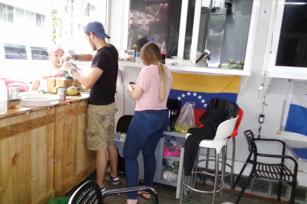 Los venezolanos Marcela Sánchez y Marcelo Román atienden a un panameño en su negocio de venta de jugos en un restaurante en la capital panameña, en el que sobresalen las banderas de Venezuela y de Panamá. (Foto: JOSÉ MELÉNDEZ - Enviado)
