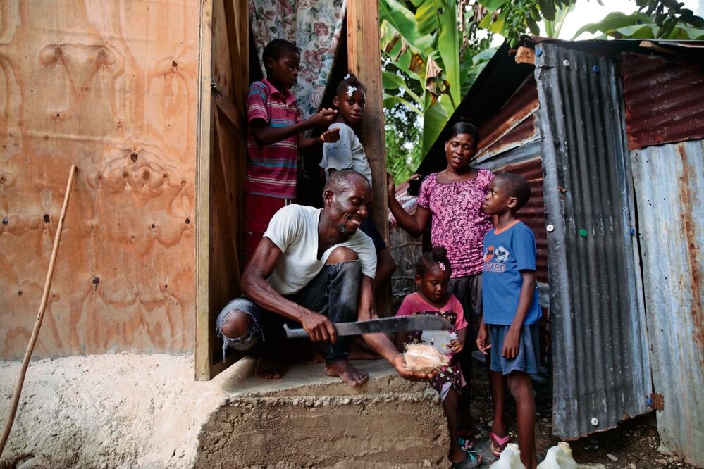 Mackenson Victor abre un coco para su hija Manouchi y sus hijastros, mientras su pareja Renese Esteve observa su casa en un zona rural de Saint-Louis-du-Sud, Haití, Foto: Odelyn Joseph / AP