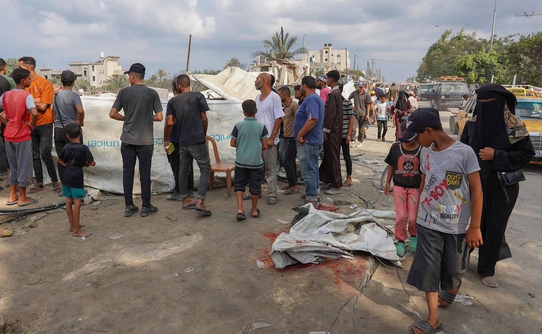 Jóvenes palestinos observan una mancha de sangre cubierta en el suelo mientras otros reacomodan una tienda de campaña en el lugar del bombardeo israelí un día antes en el campamento de desplazados de al-Mawasi. Foto: AFP