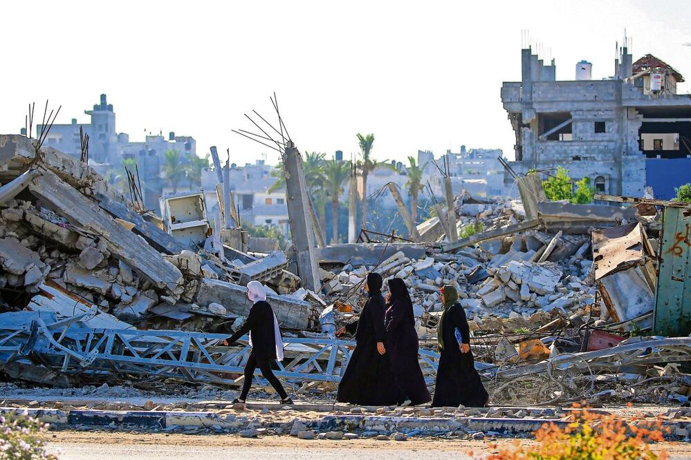 Palestinas caminan junto a edificios destruidos durante un bombardeo israelí en Gaza. Foto: Eyad Baba AFP