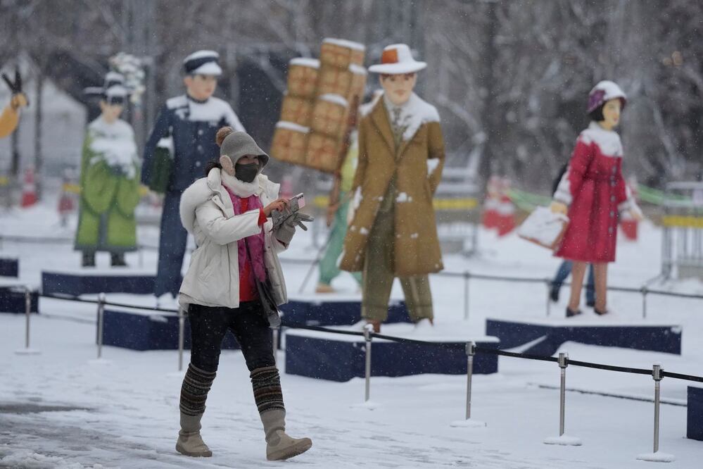 Una mujer con mascarilla sostiene su smartphone en la nieve en el centro de Seúl, Corea del Sur, el miércoles 21 de diciembre de 2022. (AP Photo/Lee Jin-man)