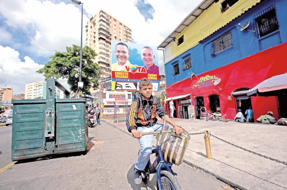 Un niño pasa en bicicleta frente a un cartel de candidatos oficialistas a las elecciones legislativas venezolanas. Encuestas dan 30 puntos de ventaja a la coalición opositora (FERNANDO LLANO. AP)