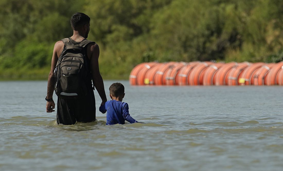 Migrantes caminan junto a grandes boyas que se utilizan como barrera fronteriza flotante en el río Bravo, en Eagle Pass, Texas. Foto: AP