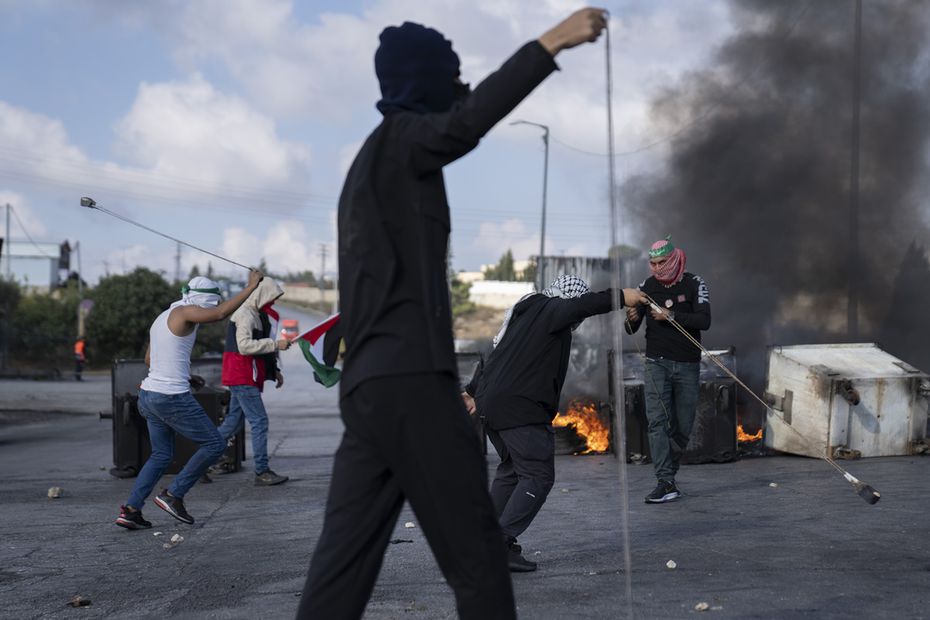 Manifestantes palestinos usan hondas detrás de neumáticos quemados durante enfrentamientos contra la policía fronteriza israelí luego de una marcha contra los bombardeos israelíes en Gaza, en la ciudad cisjordana de Ramallah. Foto: AP