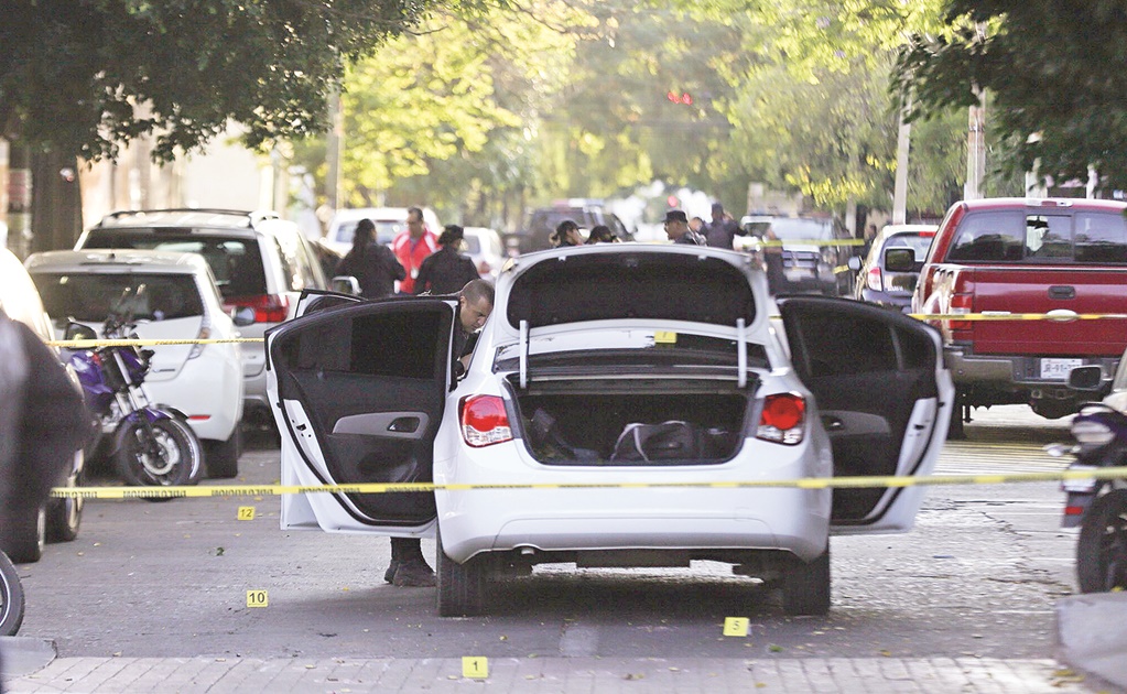Un auto blanco con las puertas y cajuela abiertos en medio de dos cintas de prohibido el paso y balas marcadas en el piso