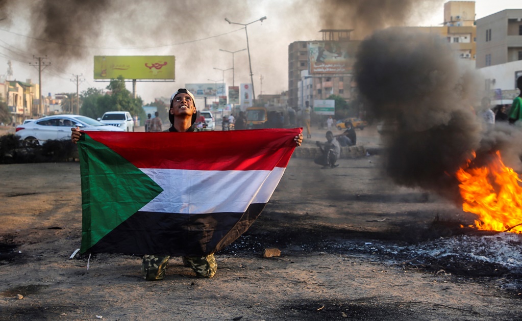Un manifestante sudanés sostiene la bandera nacional junto a neumáticos en llamas durante una manifestación en la capital, Jartum.